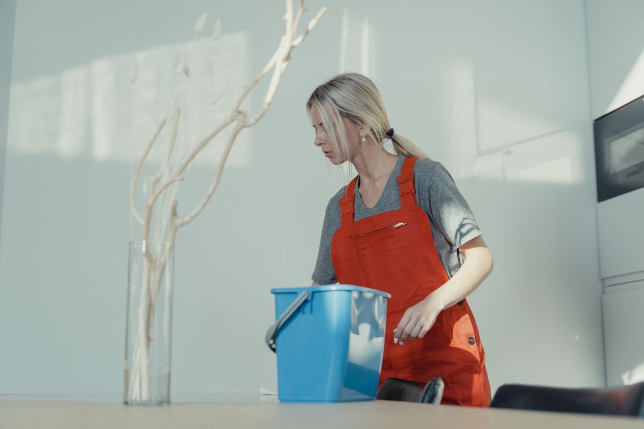 expertise-01 Žena u crvenoj uniformi čisti u unutrašnjosti uz plavu kantu, osiguravajući besprijekorno čist prostor.